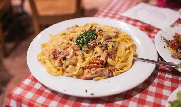 A plate of pasta on a table with a checkered tablecloth is laid out.