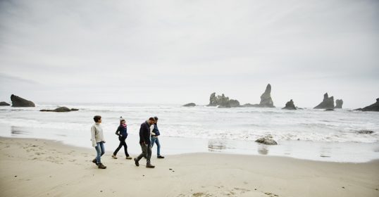 Three people walking on the beach, possibly making friends with rocks in the background.