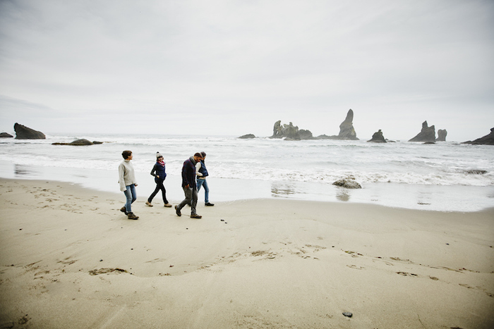 Three people walking on the beach, possibly making friends with rocks in the background.