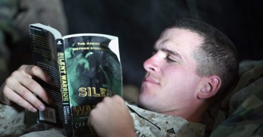 A man in a Marine Corps uniform reading a book from the Reading Lists.