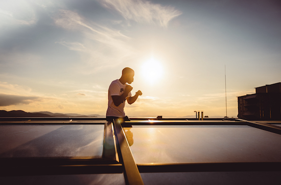 A man stands on top of a roof at sunset, casting a long shadow.