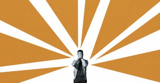 A man standing in front of a bright orange sunburst.