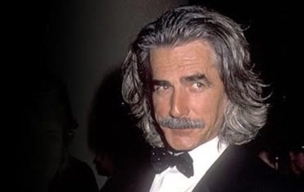 A man in a tuxedo with long hair and mustache.
