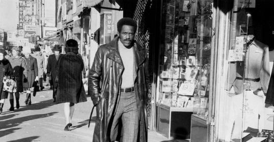 A man wearing a leather coat walks down the street.