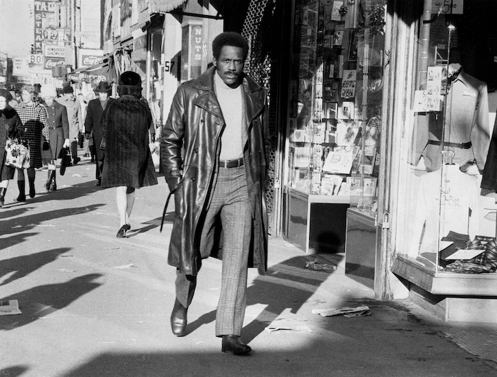 A man wearing a leather coat walks down the street.