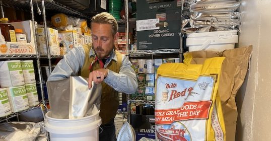 A man with a bucket in front of a shelf full of budget survival food.