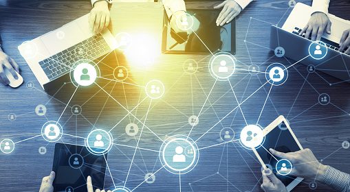 A group of people sitting around a table with laptops, overwhelmed by collaboration overload.