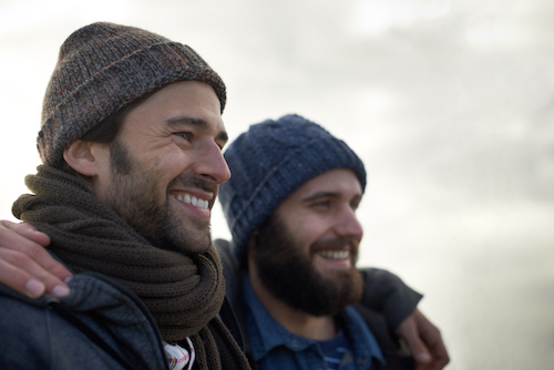 Two men with beards and hats smiling while making friends.