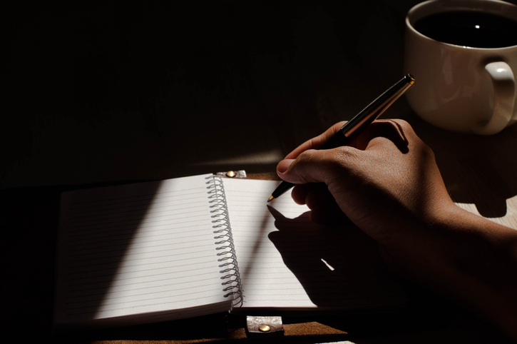 A hand writing keywords in a journal next to a cup of coffee.