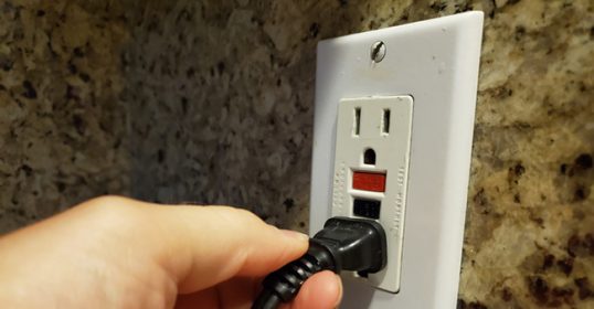 A person is holding a power cord on a GFCI outlet while working.