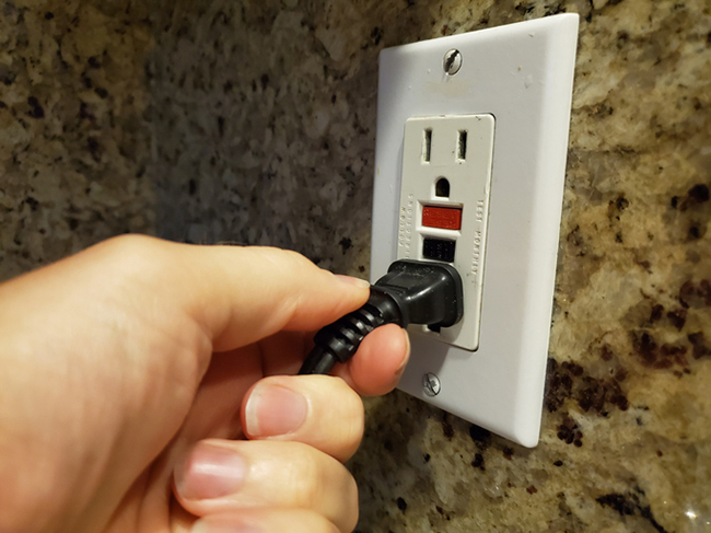 A person is holding a power cord on a GFCI outlet while working.