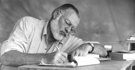 A man at a table writing a book, inspired by Ernest Hemingway.