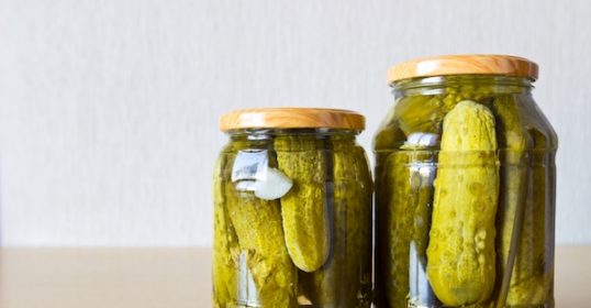 Two jars of pickles sit on a wooden table.