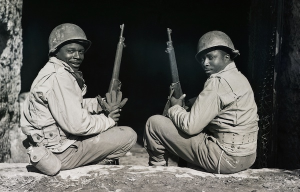 Two soldiers with rifles sitting on the ground, showcasing their willpower amidst war.