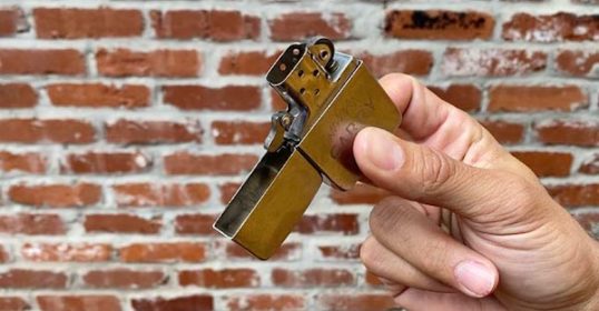 A person snapping a Zippo in front of a brick wall.
