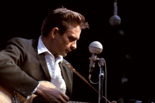 A man in a suit playing an acoustic guitar, reminiscent of Johnny Cash.