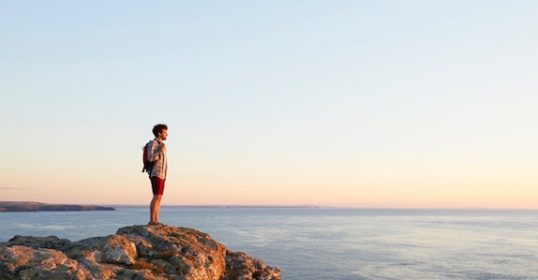 A man looking out at the ocean from the cliff top.