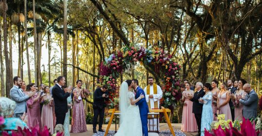 A bride and groom share a kiss under an arch in a tropical garden, representing the beauty of a wedding ceremony.