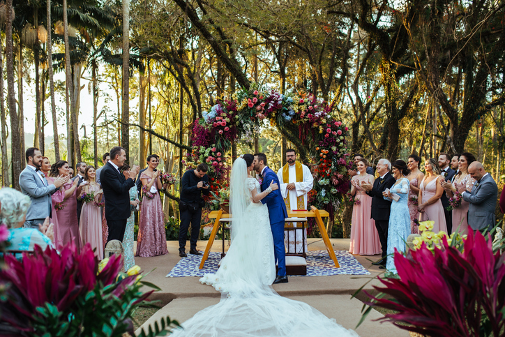 A bride and groom share a kiss under an arch in a tropical garden, representing the beauty of a wedding ceremony.