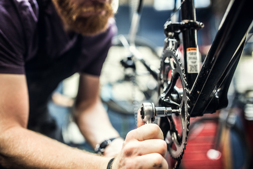 A man is conducting bike maintenance on a bicycle in a shop, possibly fixing an inner tube or applying a patch.