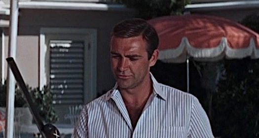 Two chill dudes standing next to a pool with a rifle.