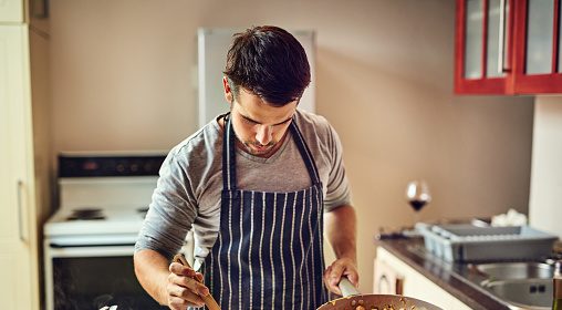 A man in an apron, chef-vetted, preparing food in a kitchen.