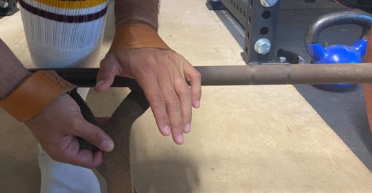 A hand is holding a barbell in a gym for strength training.
