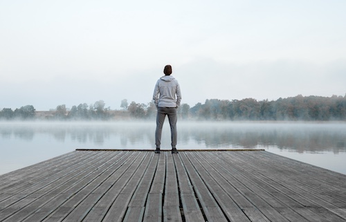 A man stands on a dock gazing at a lake during Sunday Firesides.