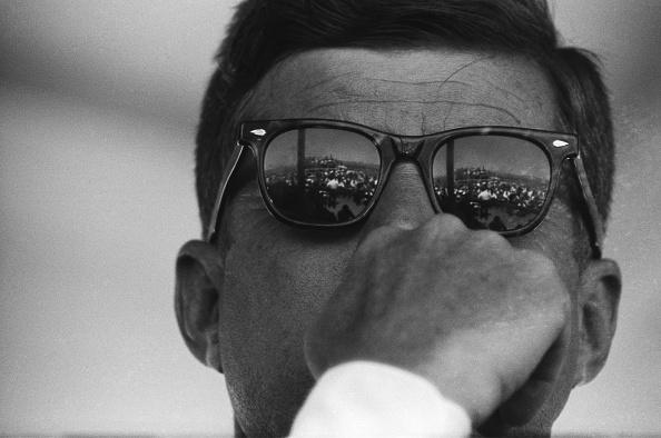 JFK's sunglasses are compellingly reflected in a mirror.