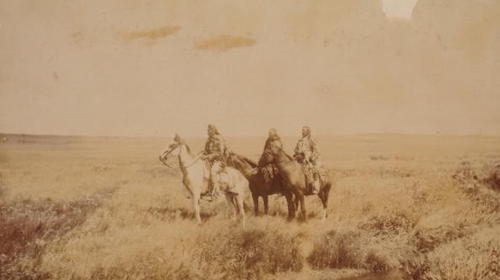 Three native American warriors on horseback near a stream.