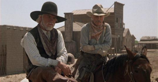 Two men in cowboy hats, one with a Podcast microphone, sitting on a horse.