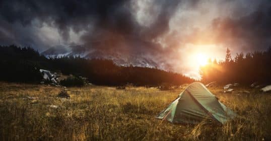 A tent is pitched in the middle of a field for dispersed camping under a cloudy sky.