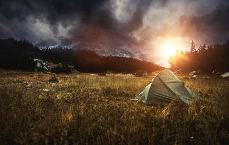 A tent is pitched in the middle of a field for dispersed camping under a cloudy sky.