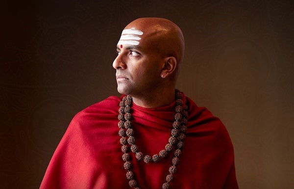 A man in a red robe with a beaded necklace exudes power and unwavering focus.