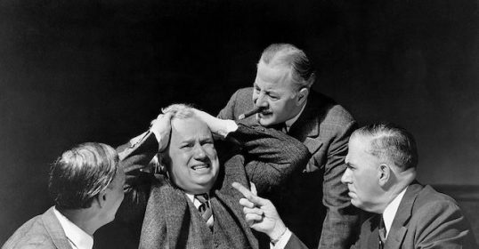 A group of highly skilled men sitting at a table with papers.