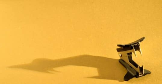 A shadow of a paper clip on a yellow background.