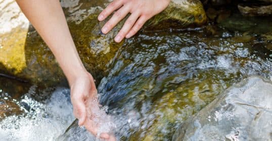 A woman is washing her hands in a stream of water with a sense of focus and efficiency.