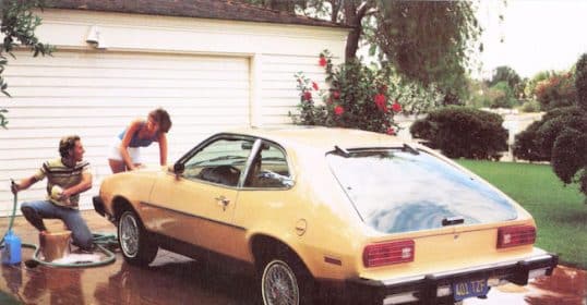 Two people protect a yellow car in a driveway.