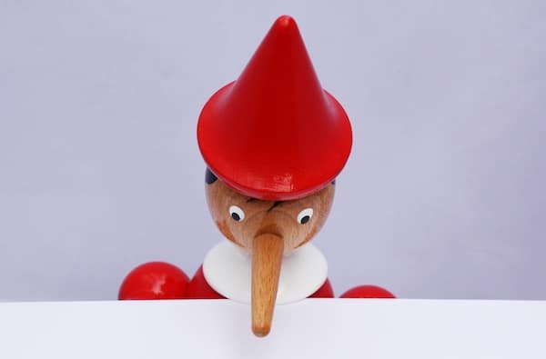A wooden elf with a red hat is standing on a white piece of paper.