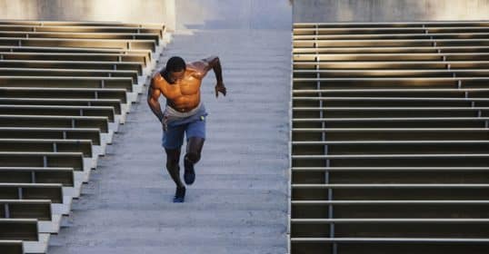 A man conditioning by running up stairs in a stadium to develop his strength.