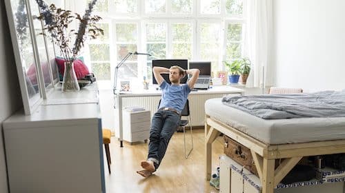 A man lays on his bed in a dorm room, seeking tranquility.