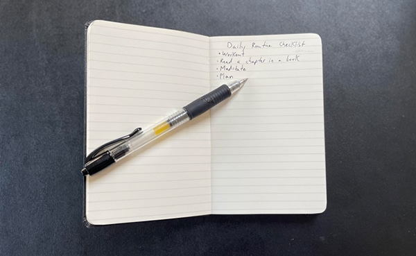 A notebook open to a page with a handwritten "Try a Daily Checklist" routine and a pen lying on top.