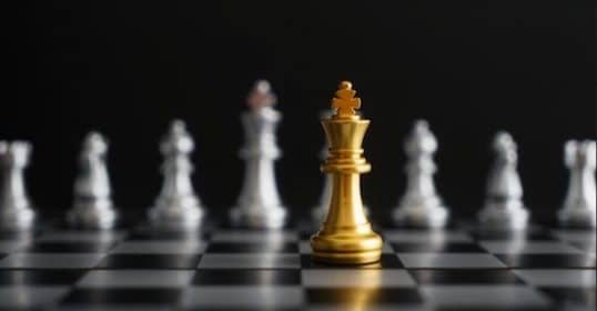 Golden king chess piece facing a line of silver pawns on a chessboard, embodying the