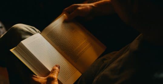 Person reading a book on the importance of cultural literacy in dim lighting.