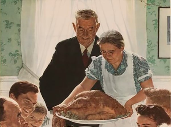 Elderly couple presenting a large turkey to a family gathered around a dinner table in their Thanksgiving outfits.