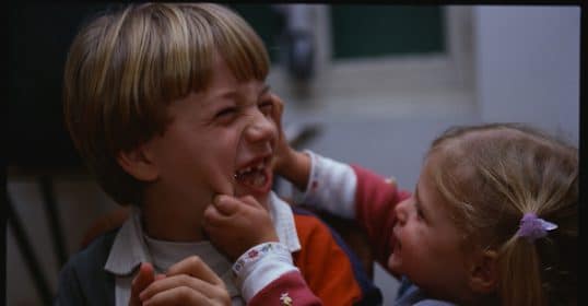 A girl playfully touches a boy's cheek as both siblings smile, demonstrating their affectionate relationship.
