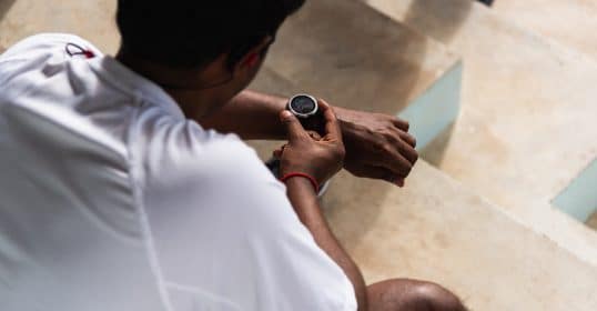 A person checking a smartwatch to monitor workout efficiency while sitting on steps.