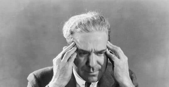 A black and white image of a man in a suit clutching his head in a gesture reflecting his struggle with emotional control.