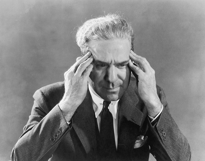 A black and white image of a man in a suit clutching his head in a gesture reflecting his struggle with emotional control.