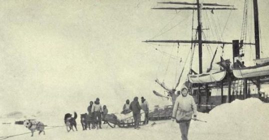 A historical black and white photo of an early Arctic Expedition with people and a sled dog team near a ship encased in ice, featured in Podcast #872 on Leadership Lessons.